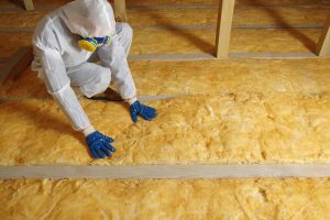 A technician presses his hands against insulation on the floor of an attic.